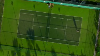 Güneşin boş yeşil tenis kortunun üzerinde batışını seyredin, sıcak renkler döküyor..