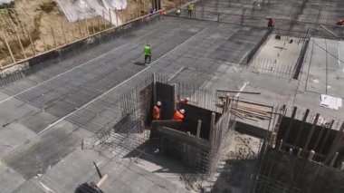 Yerleri hazırlayan ve yaklaşan inşaatın temelleri için demirleri büken işçileri gözlemleyin..