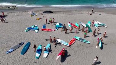 Yaz ayının ilk günü bir SUP festivali sırasında kürek çeken ve manzaralı bir koyda eğlenen bir grup izleriz..