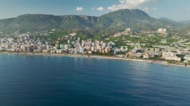 Yukarıdan, binaların mavi denizle buluştuğu, kıyı şeridini kucaklayan bir şehre bakın, hepsi kristal berraklığında 4K.