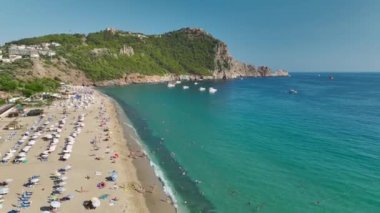 Deniz mutluluğuna tanık olun. Yat, güneşi yansıtan sularda süzülüyor. Sahilde sakin bir gün..