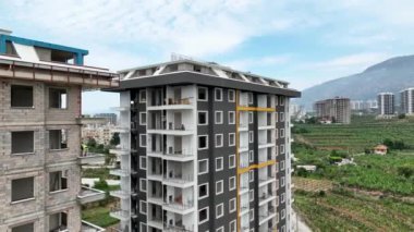 Akdeniz kıyısında dev bir bina yükseliyor, yukarıdan detaylı cephe çalışmaları görülüyor..