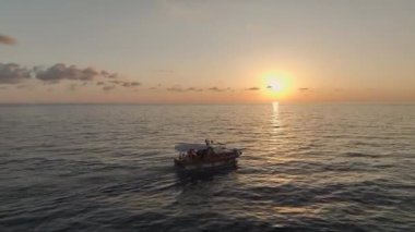 Bir balıkçı teknesi gün batımının altında süzülür.