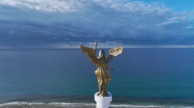 Arkasında panoramik deniz manzaralı melek heykeli.