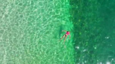 Yumuşak beyaz kumların üzerinde uzanan bikini modeline bakın, arkasında turkuaz deniz uzanıyor..