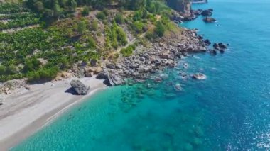 Bir grup insan sihirli bir plajda dinleniyor, raket kullanıyor ve temiz suda yüzüyor..