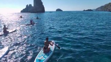 Bir grup dinlendirici bir plaj gününün tadını çıkarıyor, temiz suları olan güzel bir sahilde yüzmek ve kürek çekmek..