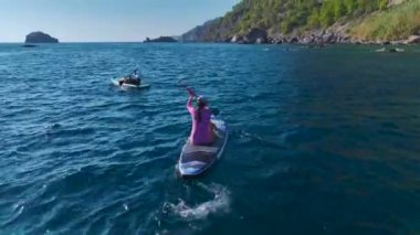 İnsanlar günlerini berrak bir plajda, yüzerek, güneşlenerek ve kürek çekerek geçiriyorlar..