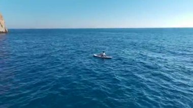 Güneşin altında yüzen, dinlenen ve kürek çeken insanların bulunduğu çarpıcı bir sahil..