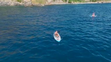 Güneşli sularda yüzen, güneşlenen ve kürek çeken insanların olduğu güzel bir sahil..