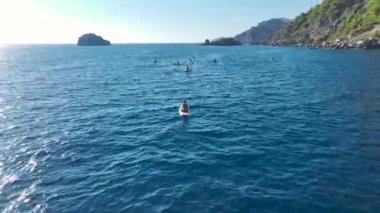 İnsanlar günlerini berrak bir plajda yüzerek, güneşlenerek ve kürek çekerek geçiriyorlar..