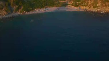 Bir grup insan sihirli bir plajda güneşli bir günün tadını çıkarıyor, kristal berrak sularda yüzüyor ve kürek çekiyor..