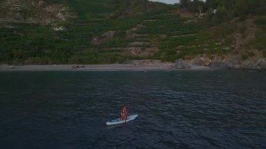 Bir manken vahşi bir plajı keşfeder, bikinili poz verir ve kıyıda kürek çeker..