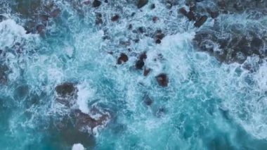 Fırtınalı dalgalar güneş doğarken kayalık kıyıya vurur ve okyanusun yüzeyinde güzel dokular yaratır..