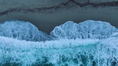 Dalgalı deniz şafak vakti kayalıklara çarpar ve okyanusun dramatik dokusunu gösterir..