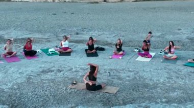 Kızlar dinlenir ve güneş batarken kayalık bir plajda yoga yapar, huzurlu bir an yaratırlar..