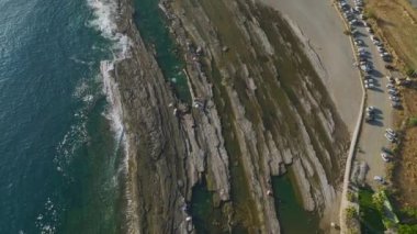 Akdeniz güneşi batarken dalgalar yavaşça kayalık bir plaja çarpar ve gökyüzünü altın renklerle doldurur..