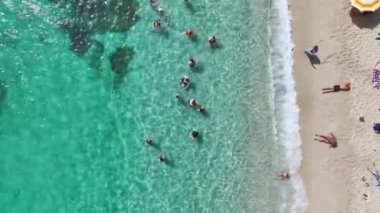 İnsanların su sporları ve plaj oyunlarıyla eğlendiği temiz, beyaz bir Akdeniz sahili..