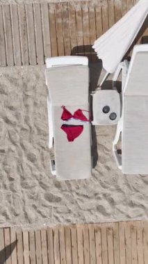 Dikey Video: Güneşin altındaki havuz başı şezlongunda kırmızı mayo.