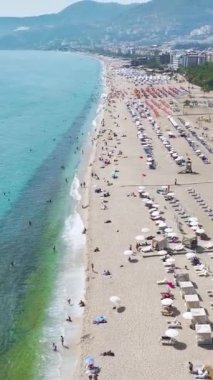 Dikey Video: Gökyüzü altındaki gök mavisi dalgalar yumuşak beyaz kuma yuvarlanıyor.