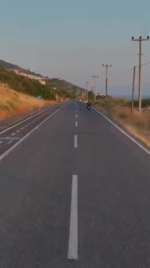 Dikey Video: Turuncu gökyüzü motosikletçilerin günbatımında sahil yolculuğu çerçevesi.