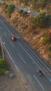 Dikey Video: Bir motosikletçi altın bir günbatımı arkaplanıyla hız yapar.