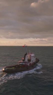 Gökyüzü gün batımının renkleriyle ve gökkuşağıyla parlarken limana yaklaşan bir deniz çekişmesi.