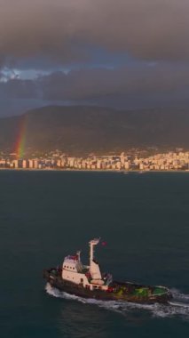 Römorkör, güneşli bir gün batımı ve gökkuşağı altında sakin denizlerde yol alır..