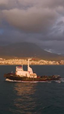 Gün batımı ve gökkuşağının gökyüzünü renklendirdiği gibi sakin sularda süzülen bir römorkör.