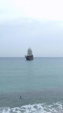 Heyecanlı turistlerle dolu korsan temalı bir gemi kıyıya yakın yelken açıyor.
