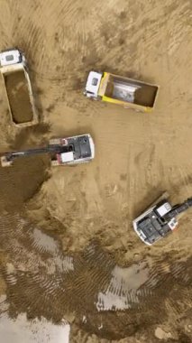 İşçiler duvarları yükseltirken ağır ekipmanlar malzemeleri kaldırır.