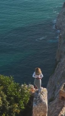 Dikey Video: Akdeniz ufkunun manzaralı Rocky Cliff üzerinde çarpıcı model pozu