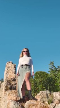 Dikey Video: Arka planda Akdeniz ile Bir Uçurumda Korkusuzca Poz Veren Model