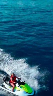 Dikey Video: Bir kız açık denizde mavi suyla jet ski sürüyor.