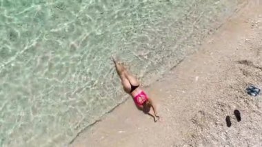 Arka planda turkuaz deniz bulunan el değmemiş beyaz bir kumsalda rahatlayan bikini modeline bakın..