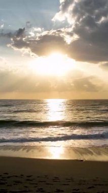 Parlayan bulutlar ve nazik dalgalarla sakin bir sahil manzarası.