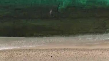 Turkuaz suların temiz bir gökyüzünün altında el değmemiş beyaz kumlarla buluştuğu sakin bir plajın nefes kesici hava perspektifini deneyimleyin..