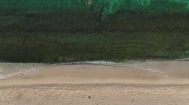 Berrak bir gökyüzünün altında turkuaz suların el değmemiş beyaz kumlarla buluştuğu sakin bir sahilin çarpıcı hava manzarasını deneyimleyin..
