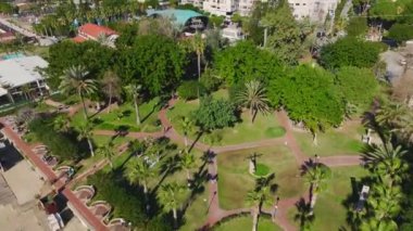 Palmiye ağaçları, dolambaçlı yollar ve Akdeniz sularının berrak manzaralı huzurlu bir sahil parkı manzarası..