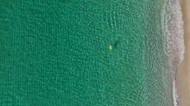 Durgun mavi denizde yüzen, berrak sularda süzülen bir adamın havadan görüntüsü..