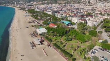 Uzun ağaçlar, yürüyüş yolları ve Akdeniz boyunca uzanan güzel deniz manzaralı bir sahil parkının insansız hava aracı görüntüleri..