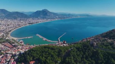 Kıyı şeridi boyunca canlı bir şehrin insansız hava aracı çekimi, arkada derin mavi bir okyanus ve parlak bir gökyüzü var..