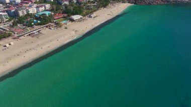 Derin mavi denizin yanında modern ve geleneksel binaların karışımı olan kıyı siluetinin insansız hava aracı görüntüsü.