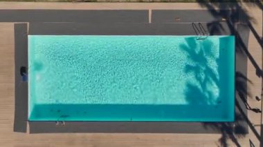 Temiz mavi suyu olan, güneş ışığını yansıtan ve huzurlu bir alanla çevrili güzel bir yüzme havuzu..