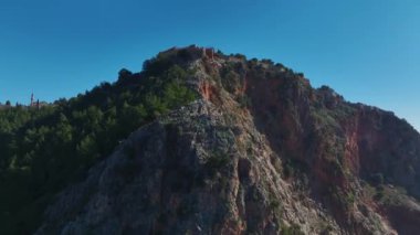 Alanya Kalesi 'nin insansız hava aracı görüntüleri. Etrafı tarihi duvarlarla çevrili ve gökyüzünün altındaki sonsuz mavi denize bakıyor..
