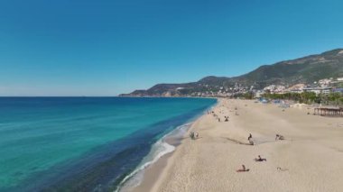 Alanya 'nın sahil şeridinin havadan çekilmiş görüntüleri, berrak mavi suyu, uzun kumlu bir sahili ve huzurlu bir yaz havasını gösteriyor..