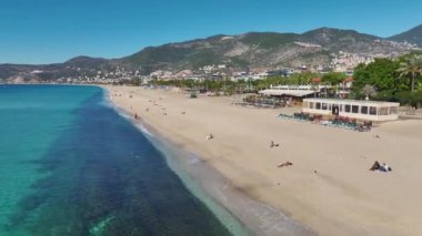 Derin mavi su, yumuşak kum ve sakin bir atmosferle Alanya sahilinin insansız hava aracı görüntüsü..