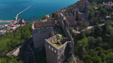 Derin mavi denize bakan kayalık bir uçurumun üzerinde taş duvarları olan antik bir kalenin insansız hava aracı görüntüleri..