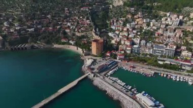 Alanya 'nın küçük limanındaki kırmızı kuleyi ziyaret edin, taş duvarlar ve arka planda manzaralı bir dağ manzarası ile çevrili..