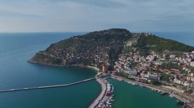 Alanya 'daki tarihi kırmızı kuleyi keşfedin, taş duvarlar, büyüleyici liman manzarası ve çarpıcı dağ manzarası.